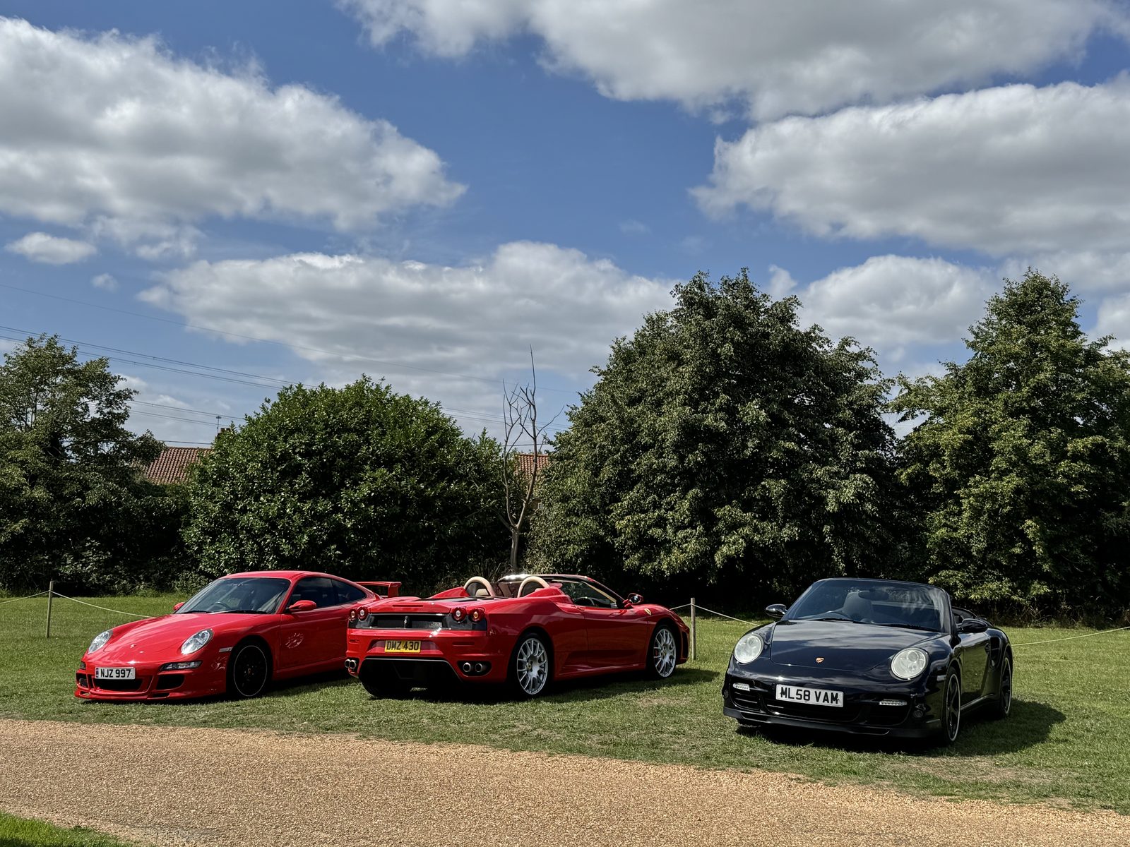 Three cars parked on the grass at Duration, West Acre, under a blue sky